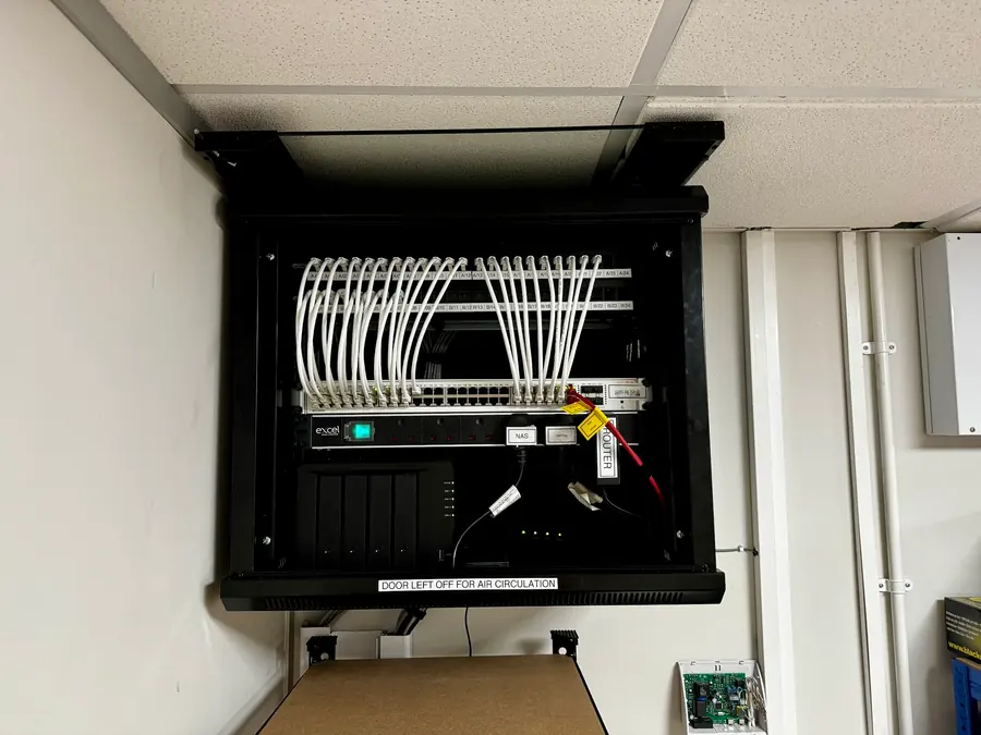 After: a wall-mounted cabinet with labelled patch panels, combed leads and labelled router, switch and NAS