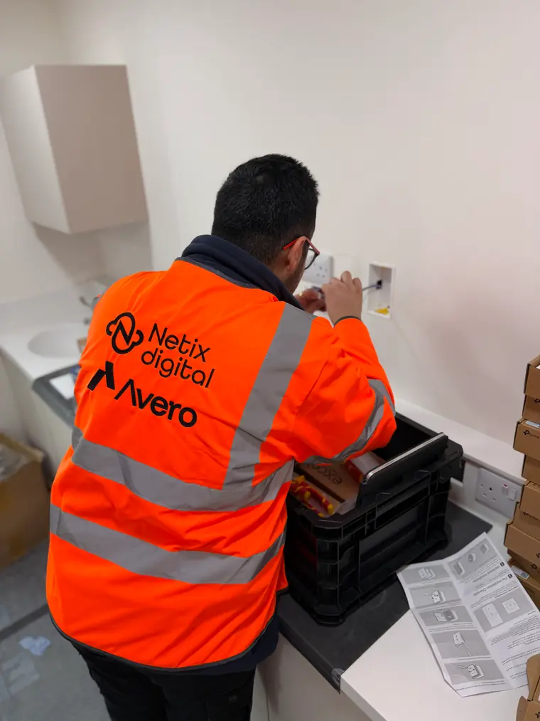 A Netix Digital engineer in branded hi-vis terminating a data outlet on a fit-out site, tool crate and TP-Link boxes beside him