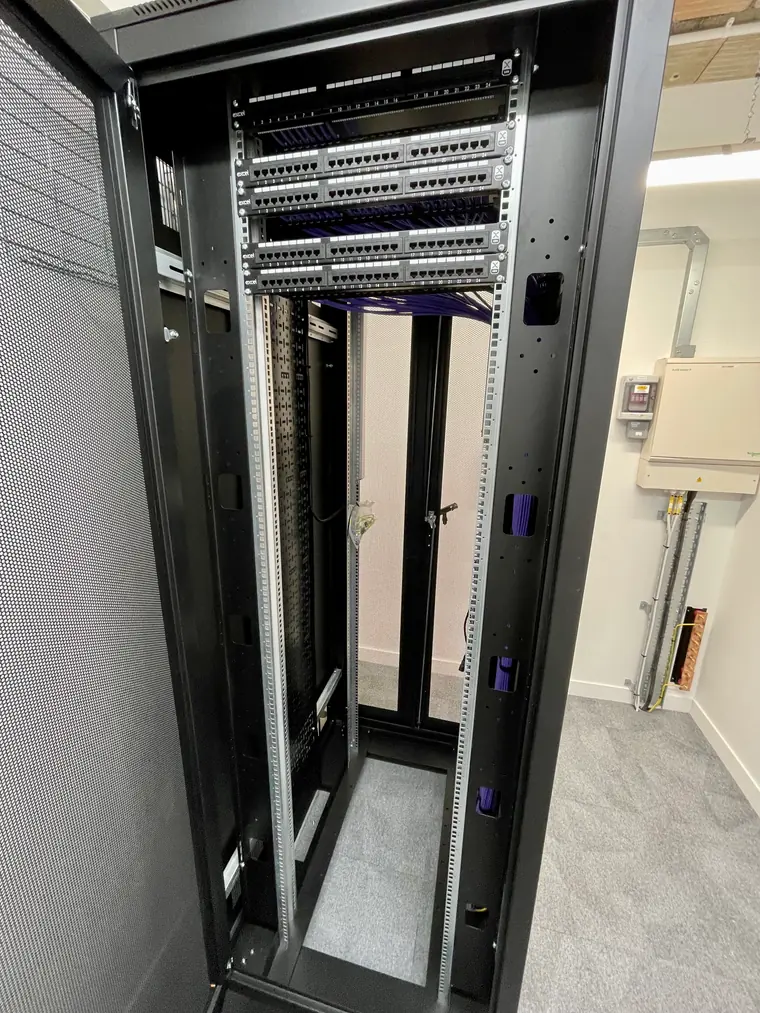 A floor-standing comms rack during installation with five 24-port patch panels terminated and violet cabling dressed behind them