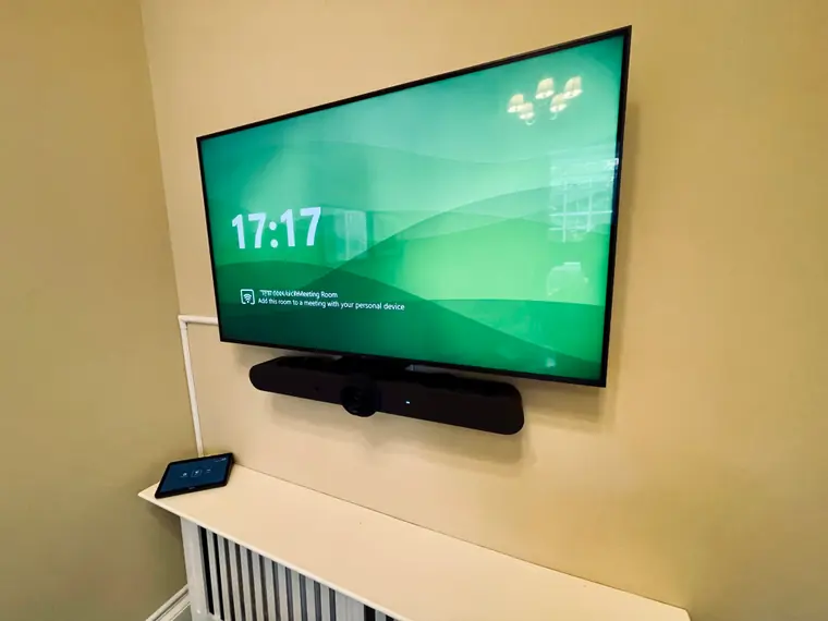 After: the same wall with a Microsoft Teams Rooms display, a Logitech video bar mounted beneath it, a touch controller on the side, and the cabling run in white trunking